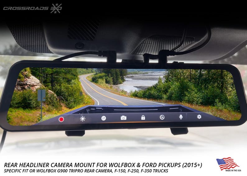 May include: A black rear view mirror with a built-in camera displaying a scenic road view. The mirror has a touch screen with icons and is mounted on a vehicle's windshield. Text at the bottom reads "REAR HEADLINER CAMERA MOUNT" and "MADE IN THE USA."