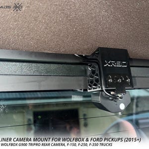 May include: Black rear headliner camera mount for Wolfbox and Ford pickups. The mount is attached to the vehicle's headliner and includes the text "XRE3". The image also includes the text "REAR HEADLINER CAMERA MOUNT FOR WOLFBOX & FORD PICKUPS (2015+)".