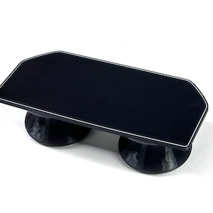 May include: A black serving tray with a white trim, supported by two rounded, dark grey bases. The tray has a rectangular shape with a modern design, suitable for serving food or displaying items.