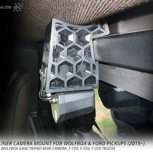 May include: A black rear headliner camera mount with a honeycomb design, designed for Wolfbox and Ford pickups. The mount is shown installed in a vehicle. The text on the image reads "REAR HEADLINER CAMERA MOUNT FOR WOLFBOX & FORD PICKUPS (2015+)".