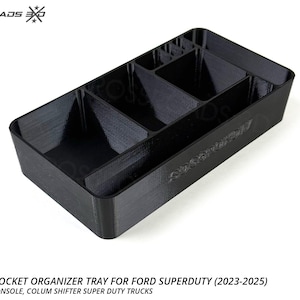May include: Black console pocket organizer tray for Ford Super Duty trucks. The tray has multiple compartments for organizing items. The text on the tray reads "Crossroads EXO" and "Super Duty". Made in the USA.