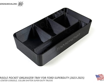Op de afbeelding: Zwarte console pocket organizer tray voor Ford Super Duty trucks. De tray heeft meerdere compartimenten voor het organiseren van items. De tekst op de tray luidt "Crossroads EXO" en "Super Duty". Gemaakt in de VS.