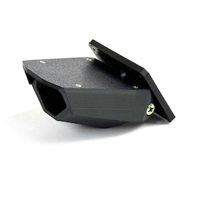 Może przedstawiać: Czarny, kątowy wspornik z teksturowaną powierzchnią i prostokątną płytą montażową. Wspornik ma sześciokątny otwór i jest mocowany śrubami. Projekt jest nowoczesny i przemysłowy.