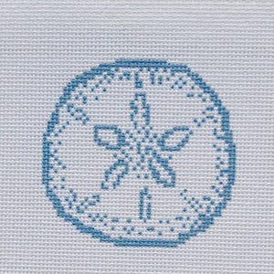 May include: A blue cross-stitch design of a sand dollar on a white background. The sand dollar is a circular shape with a detailed, symmetrical pattern in the center. The design is on a textured, woven fabric.