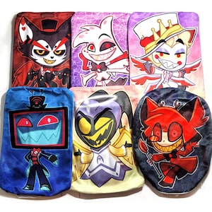 May include: Six plush pillows featuring characters from the animated series "Hazbin Hotel". The pillows are all different colors and feature different characters, including a red demon with horns, a blue robot with a screen for a head, and a yellow angel with wings.