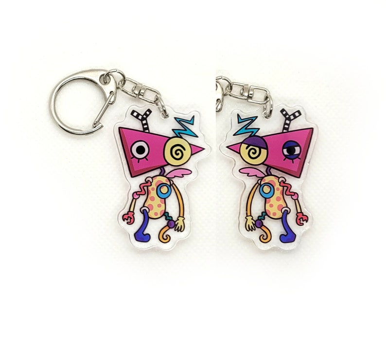 May include: Two colorful cartoon character keychains with pink, yellow, blue, and black details. The characters have large eyes and are attached to silver key rings.