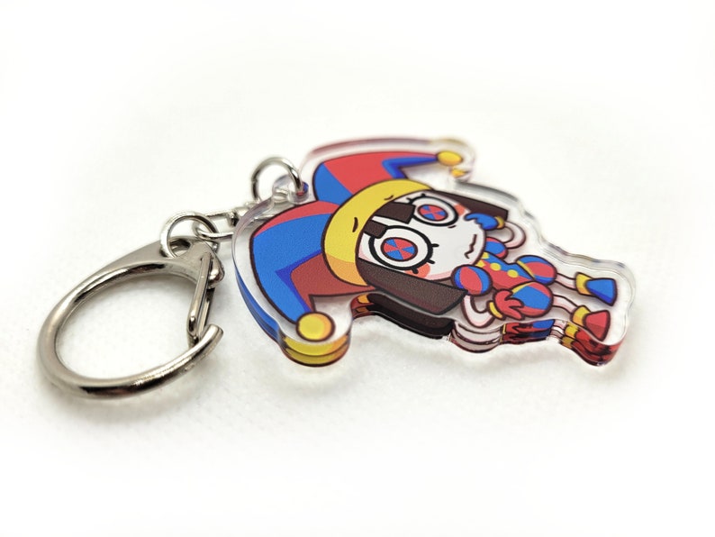 May include: A colorful jester character keychain with a red, yellow, and blue jester hat, white face, and red and blue clothing. The keychain is attached to a silver metal ring.