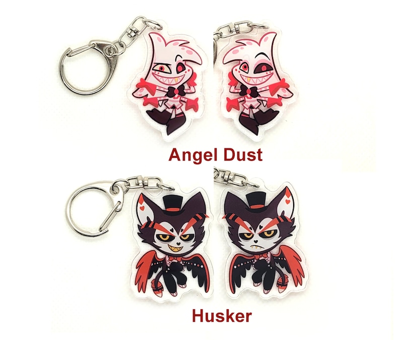 Puede incluir: Dos llaveros con personajes de la serie animada Hazbin Hotel. El primer llavero presenta a Angel Dust, un demonio rosa y blanco con cuernos rojos y una corbata de mo&ntilde;o roja. El segundo llavero presenta a Husker, un demonio negro y rojo con un sombrero de copa y alas rojas. Ambos llaveros est&aacute;n sobre un fondo blanco.
