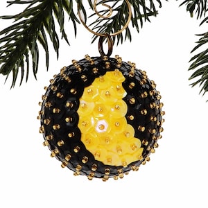 May include: A black and yellow Christmas ornament covered in sequins. The ornament is shaped like a sphere and has a gold hanger.