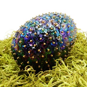 May include: A large iridescent egg covered in sequins and gold beads, nestled in a bed of green moss.