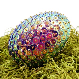 May include: A iridescent purple, green, and gold Easter egg covered in sequins. The egg is sitting in a bed of green moss.