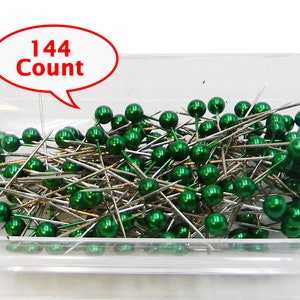 May include: A clear plastic container filled with 144 green headed sewing pins. The container is labeled "144 Count".