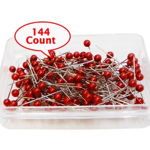 May include: A clear plastic container filled with 144 red headed sewing pins. The container has a white label with the text "144 Count".