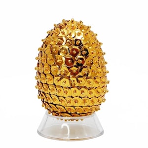 May include: A gold egg-shaped ornament covered in sequins, sitting on a clear plastic stand.