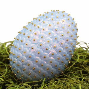 May include: A light blue Easter egg covered in iridescent sequins and gold beads, nestled in a bed of green moss.
