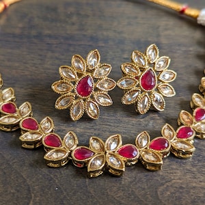 May include: A gold necklace with a delicate design featuring red gemstones and clear rhinestones. Matching earrings with a similar design are also included.