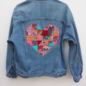 May include: A blue denim jacket with a large patchwork heart on the back. The heart is made of various colourful fabrics, including red, pink, green, and blue.