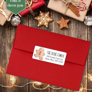 May include: A red envelope with a white label featuring a gingerbread man illustration and the text "THE CLYDE FAMILY 345 Candy Cane Ln. Santa Way, NP 12345".