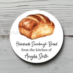 May include: A white round sticker with a watercolor illustration of a loaf of sourdough bread. The text on the sticker reads "Homemade Sourdough Bread from the kitchen of Angela Smith."