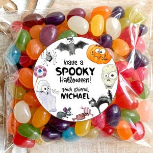 May include: A clear plastic bag filled with colorful jelly beans. A round sticker with a Halloween theme is attached to the bag. The sticker features a variety of spooky characters, including a ghost, a bat, a spider, a pumpkin, and a skull. The text on the sticker reads "Have a Spooky Halloween! Boo! Your friend, Michael."