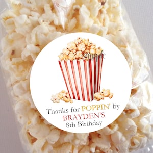 May include: A clear cellophane bag filled with popcorn. A round sticker on the bag features a watercolor illustration of a popcorn container with red and white stripes and popcorn. Text on the sticker reads "Thanks for POPPIN' by BRAYDEN'S 8th Birthday."