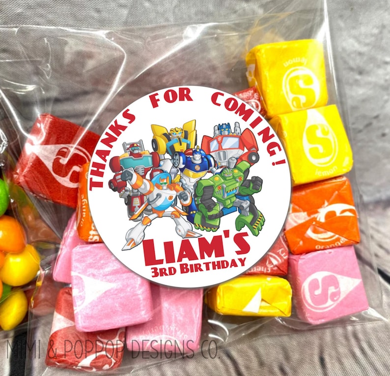 May include: A round, white sticker with a red border and the text "Thanks for coming! Liam's 3rd Birthday" in red. The sticker features a group of Transformers characters, including Optimus Prime, Bumblebee, and others.