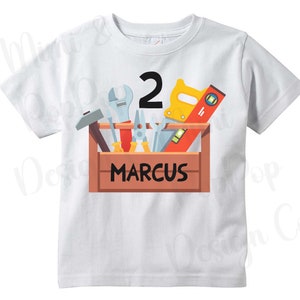 May include: White t-shirt with a cartoon image of a toolbox with tools and the number 2. The name "MARCUS" is written on the toolbox.