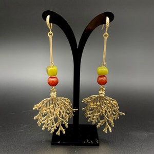 Può includere: Orecchini dorati con un designo a foglia e accenti di pietre preziose rosse e verdi.
