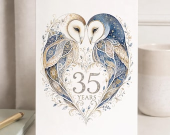 May include: A white greeting card featuring two barn owls facing each other, their bodies forming a heart shape. The owls are decorated with intricate blue and gold patterns. The text 35 YEARS is centered within the heart. The design includes delicate floral and star motifs.