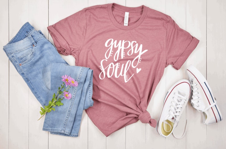 Puede incluir: Una camiseta color malva con el texto "gypsy soul" en letras blancas con un peque&ntilde;o coraz&oacute;n rosa. La camiseta se combina con unos vaqueros azules y zapatillas blancas.