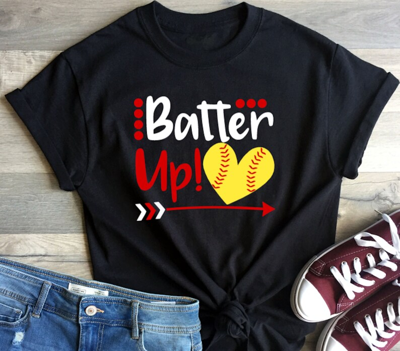 May include: Black t-shirt with white text that says "Batter Up!" and a red arrow pointing to the right. A yellow softball in the shape of a heart is above the arrow.
