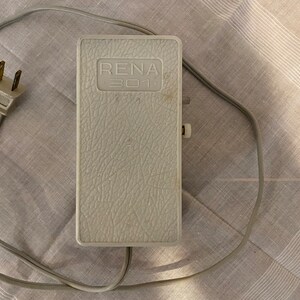 May include: A gray foot pedal with a cord and plug. The pedal has the text "RENA 301" printed on it.