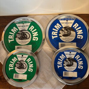 May include: Four circular Range Kleen Trim Rings with silver rims. Two rings have green centers, and two have blue centers. Each ring has the words "Trim Ring" in white, and a product label with text and a diagram.