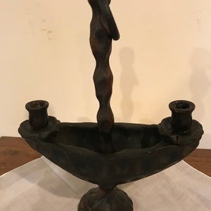Puede incluir: Un candelero de madera marr&oacute;n oscuro con dos portavelas y un asa. El candelero tiene un dise&ntilde;o &uacute;nico con una base curva y un asa retorcida.
