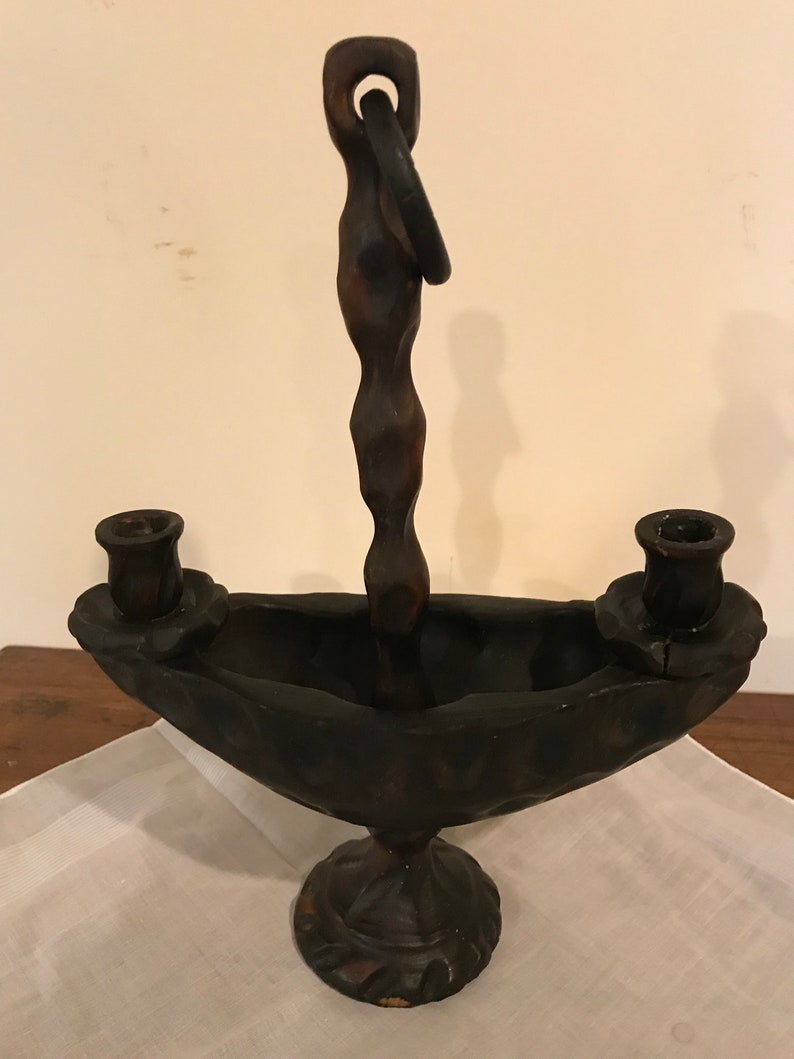 Puede incluir: Un candelero de madera marr&oacute;n oscuro con dos portavelas y un asa. El candelero tiene un dise&ntilde;o &uacute;nico con una base curva y un asa retorcida.