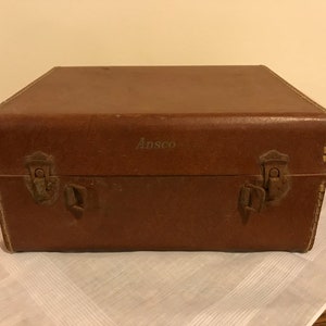 May include: A brown leather case with metal clasps and the word "Ansco" embossed on the top.