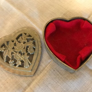May include: A silver heart-shaped trinket box with an intricate design of birds and flowers. The box is open and lined with red velvet.