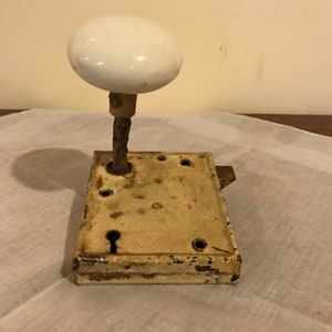 May include: Antique white porcelain door knob with a metal spindle and a brass latch. The door knob is attached to a metal door plate with a keyhole.