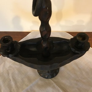 Puede incluir: Un candelero de madera negro con un dise&ntilde;o &uacute;nico. El candelero tiene tres portavelas y un poste central retorcido y decorativo.