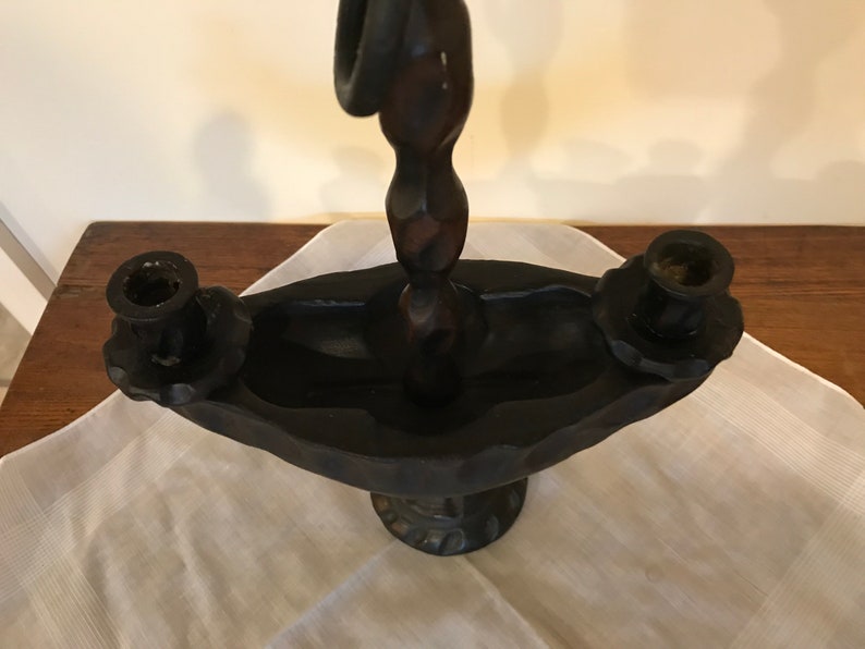 Puede incluir: Un candelero de madera negro con un dise&ntilde;o &uacute;nico. El candelero tiene tres portavelas y un poste central retorcido y decorativo.