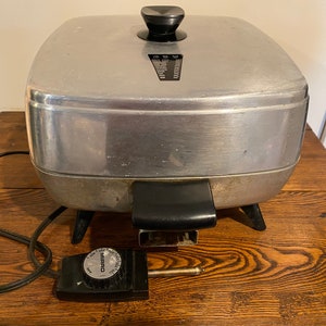 Puede incluir: Una sartén eléctrica plateada con un mango negro y un mando de control de temperatura negro. La sartén tiene un cable y un enchufe negros. La marca "MIRRO" es visible en el mando de control de temperatura.
