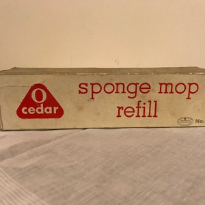 Puede incluir: Una caja de cartón blanca con texto rojo que dice "O cedar sponge mop refill No. 76". La caja tiene un triángulo rojo con una "O" blanca y la palabra "cedar" dentro.