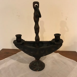Puede incluir: Un candelero de madera marr&oacute;n oscuro con dos portavelas y un lazo para colgar. El candelero est&aacute; tallado con un dise&ntilde;o &uacute;nico y tiene una base que se asemeja a un barco.