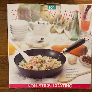 May include: A 10-inch stir fry wok with a black non-stick coating and a wooden handle. The wok is designed for professional use and can be used on gas or electric stoves. The packaging features a photo of the wok with stir-fried noodles and vegetables.
