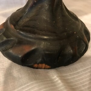 Puede incluir: La base de una figurita de cer&aacute;mica marr&oacute;n oscuro con un borde texturizado y festoneado. La base tiene un peque&ntilde;o astillado en la parte inferior.