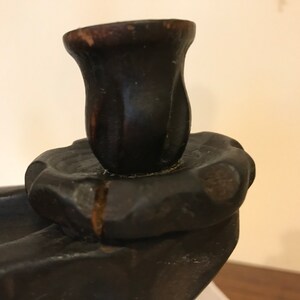 Puede incluir: Un candelero de madera marr&oacute;n oscuro con un solo portavelas. El portavelas tiene forma de capullo de flor y tiene un acabado ligeramente desgastado.