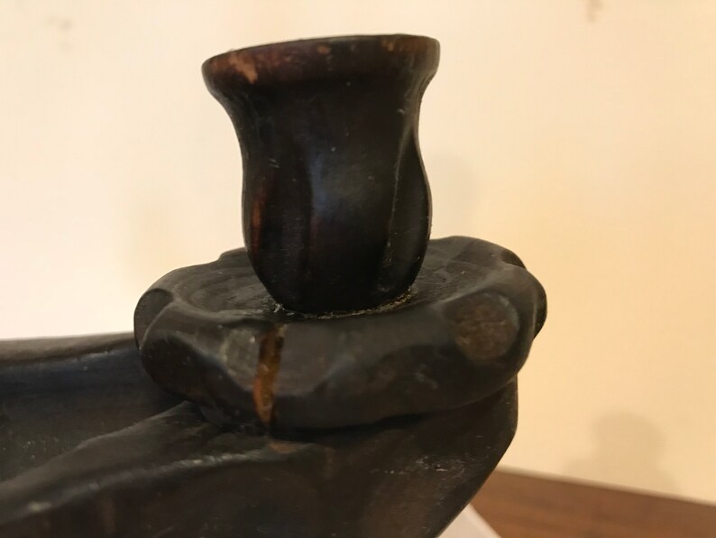 Puede incluir: Un candelero de madera marr&oacute;n oscuro con un solo portavelas. El portavelas tiene forma de capullo de flor y tiene un acabado ligeramente desgastado.
