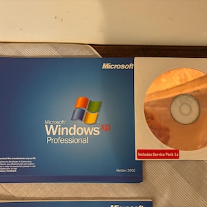 Op de afbeelding: Een Microsoft Windows XP Professional softwarepakket. De blauwe doos heeft het Windows-logo en de tekst "Windows XP Professional". Inclusief een cd-rom met "Includes Service Pack 1a" gedrukt op de witte hoes.