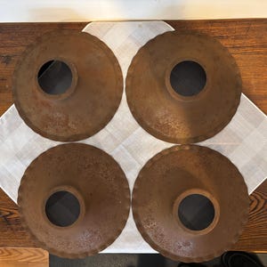 May include: Four rusty metal lampshades with scalloped edges and a central hole. The lampshades are arranged in a square pattern on a white surface.