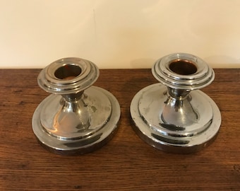 Puede incluir: Dos candelabros de plata con base redonda y centro elevado. Los candelabros tienen un acabado liso y pulido.